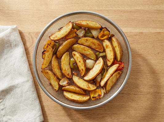 Panier de friteuse à air garni de quartiers de pommes de terre et de légumes rôtis